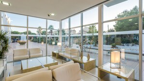 Un espace intérieur moderne doté de grandes fenêtres, d’un coin salon avec des canapés et des tables, et offrant une vue sur la terrasse extérieure.