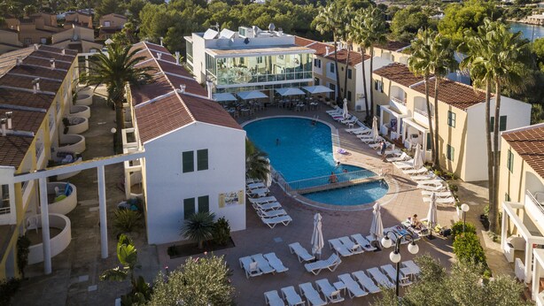 Un complexe hôtelier doté d’une piscine centrale, de chaises longues et offrant une vue sur la mer.