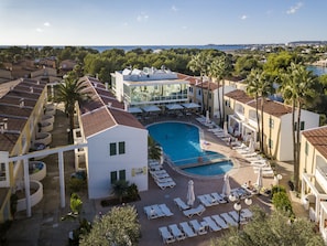 Un complexe hôtelier doté d’une piscine centrale, de chaises longues et offrant une vue sur la mer.