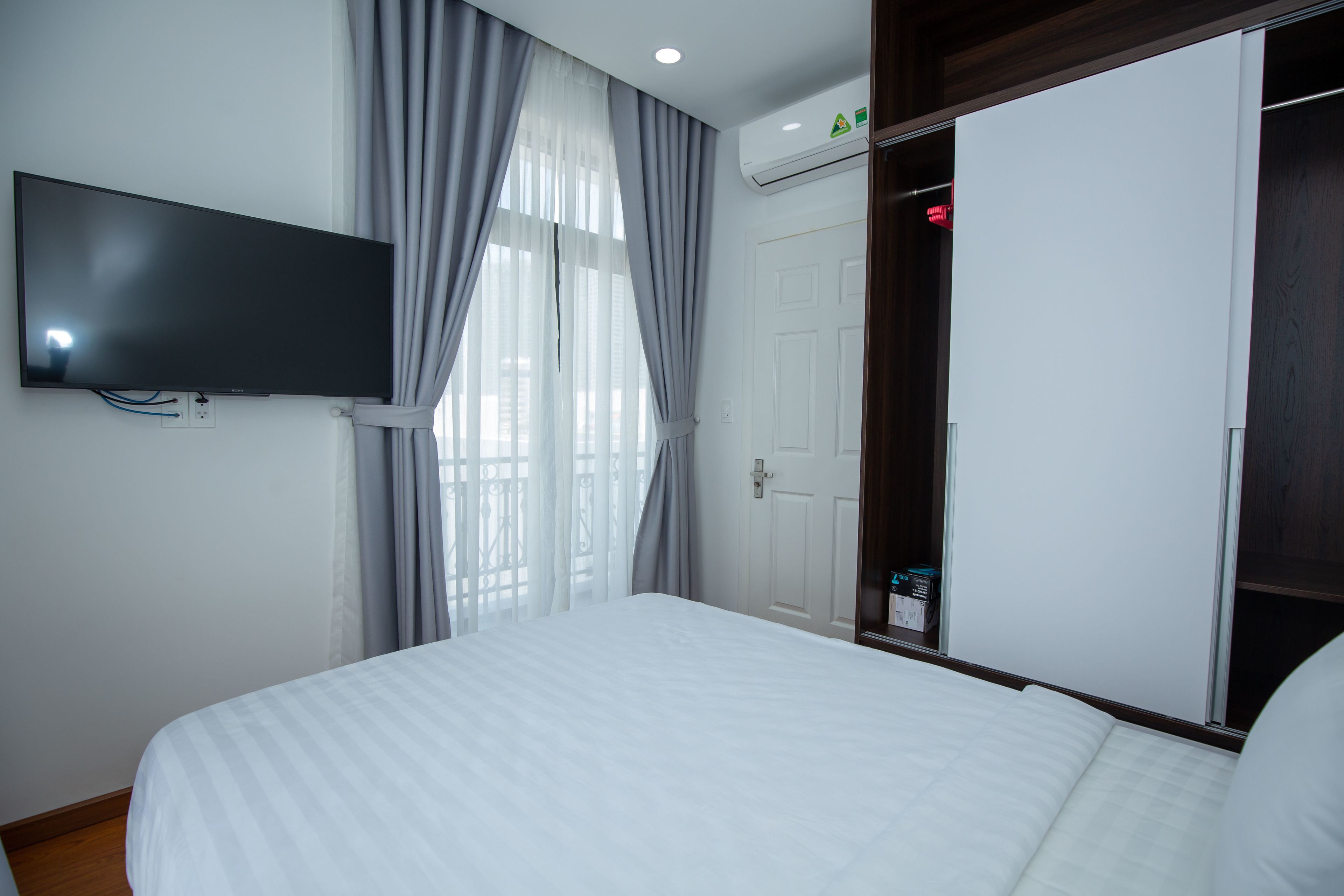 A hotel room with a bed, a television mounted on the wall, a door, and an air conditioning unit.