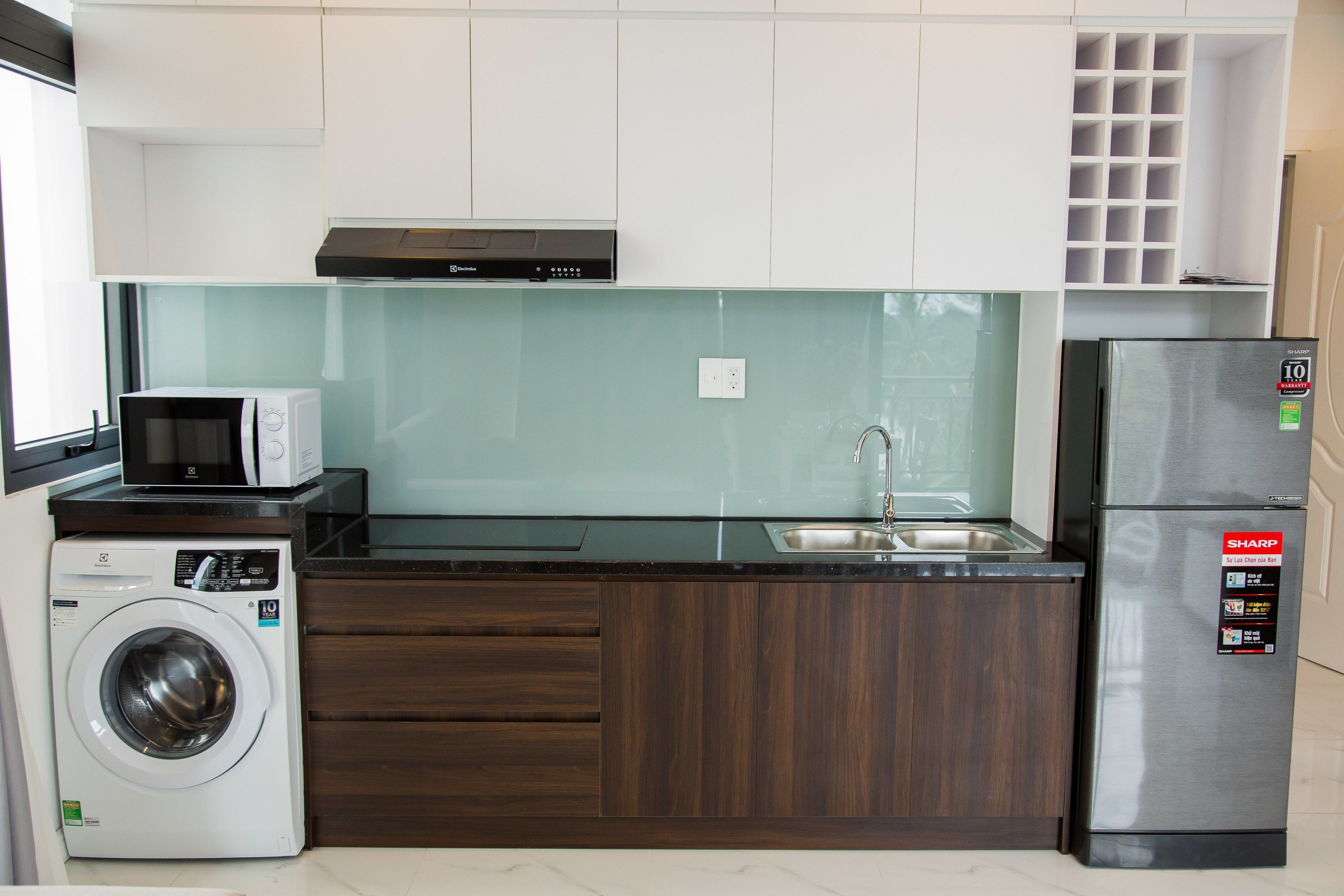 A compact kitchen with a washing machine, microwave, and refrigerator.