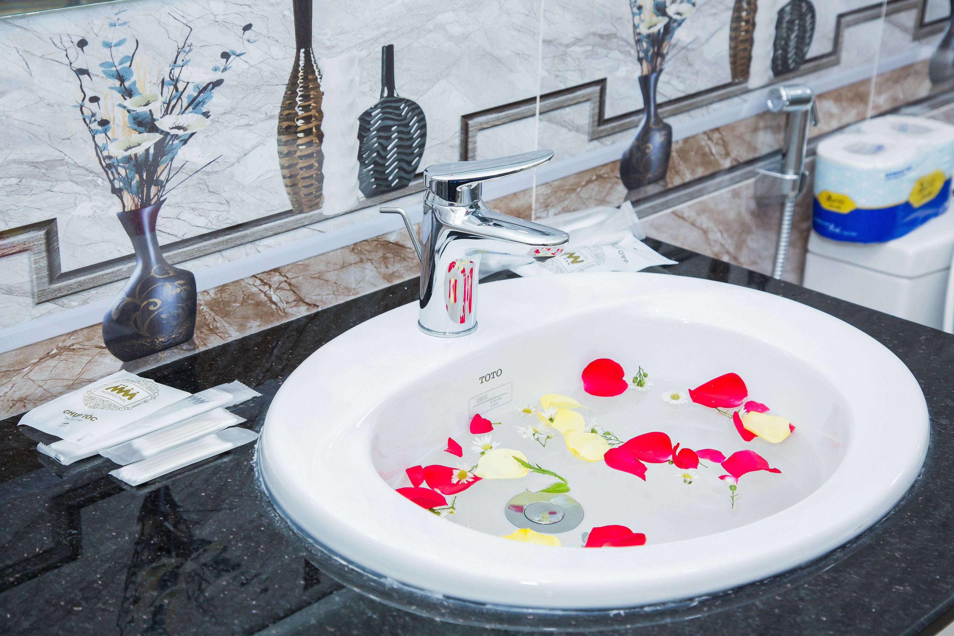 A bathroom sink with a marble countertop, a chrome faucet, and a vase with dried flowers.