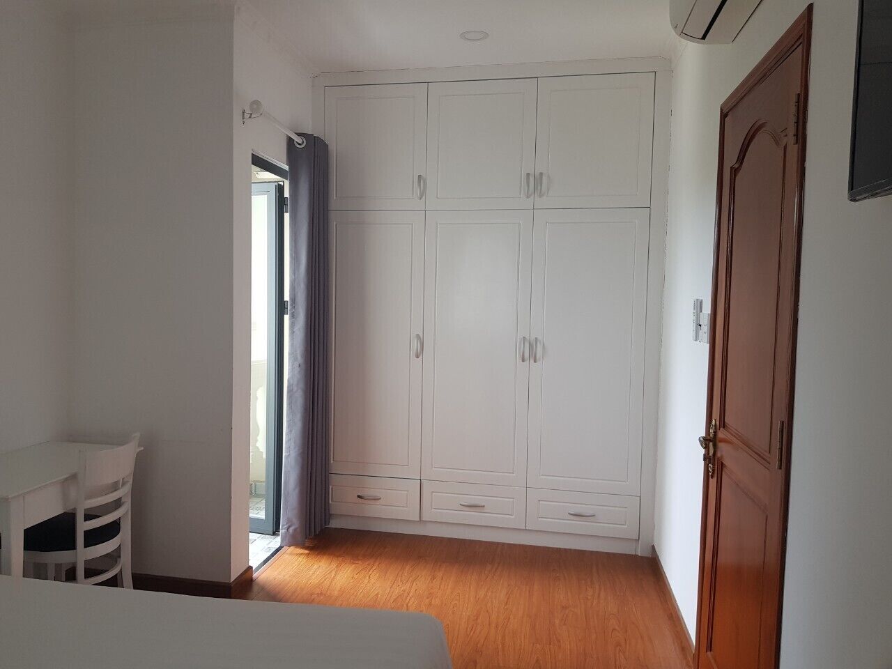 Una habitación con suelo de madera, un armario blanco y una pequeña mesa con sillas.