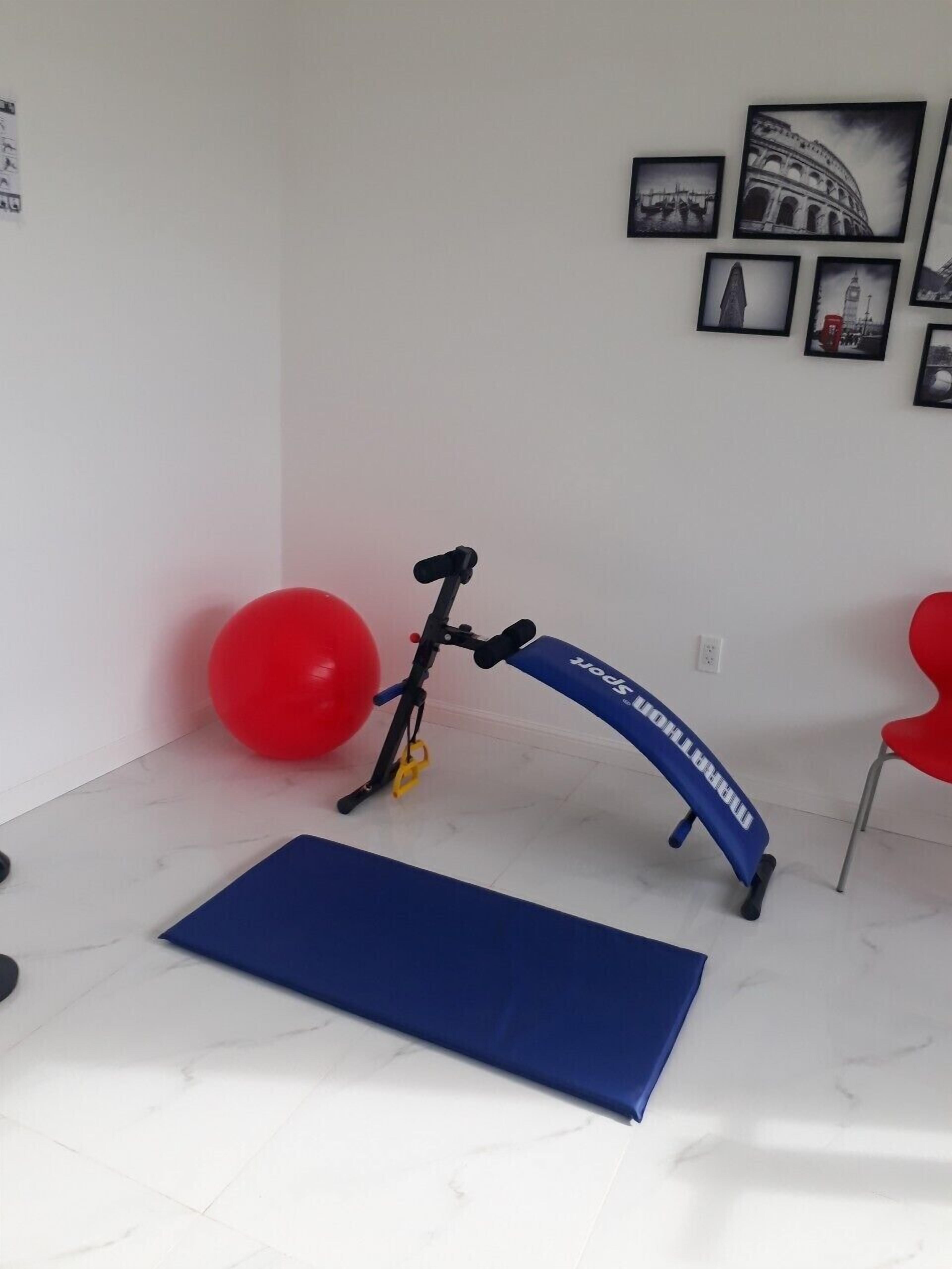 A room with a blue exercise mat, a red exercise ball, and a blue exercise bike.