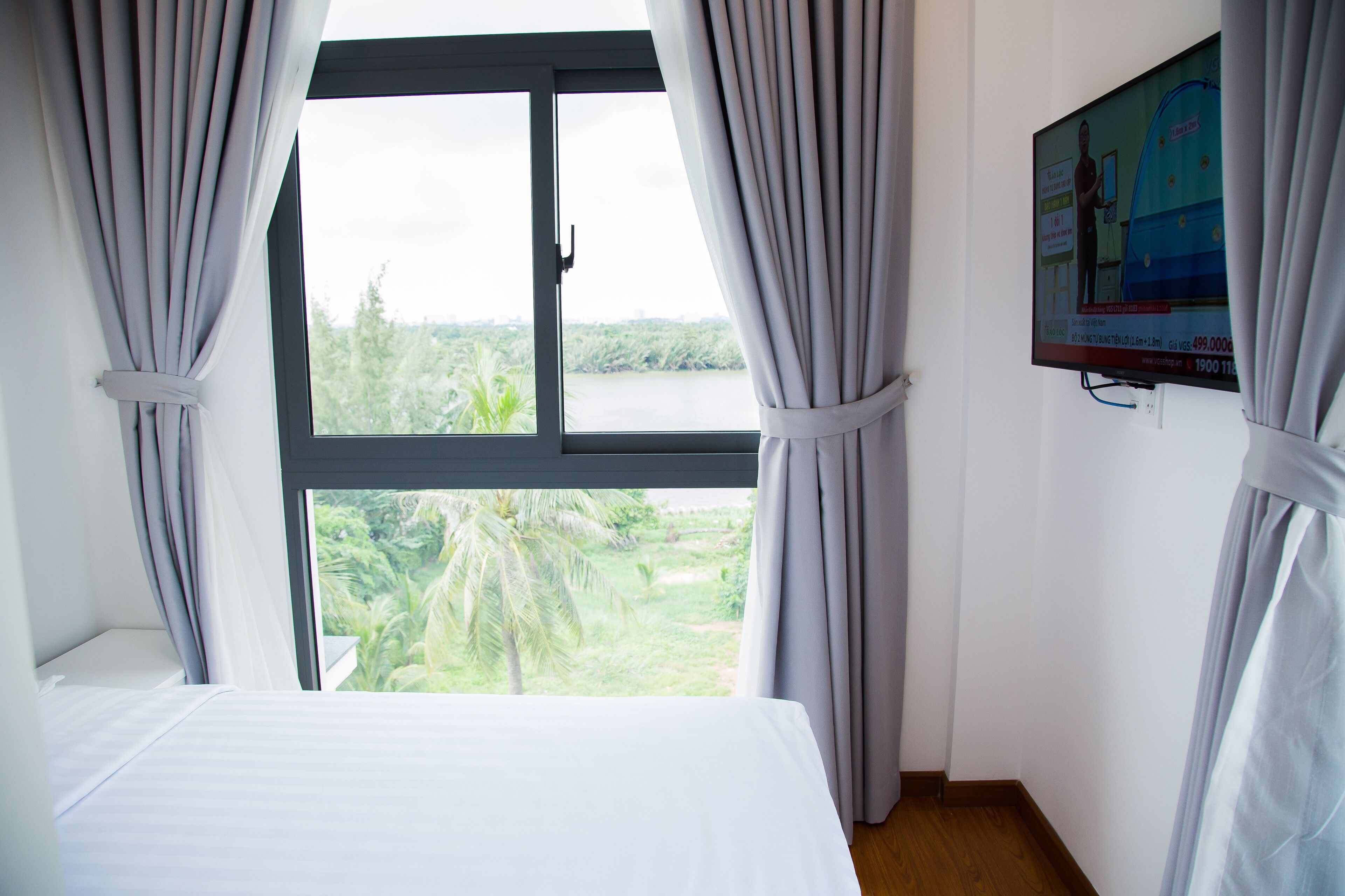 A bedroom with a large window, curtains, a bed, and a TV on the wall.