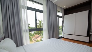 Ein Schlafzimmer mit einem großen Bett, einem Kleiderschrank und Blick auf Palmen durch das Fenster.
