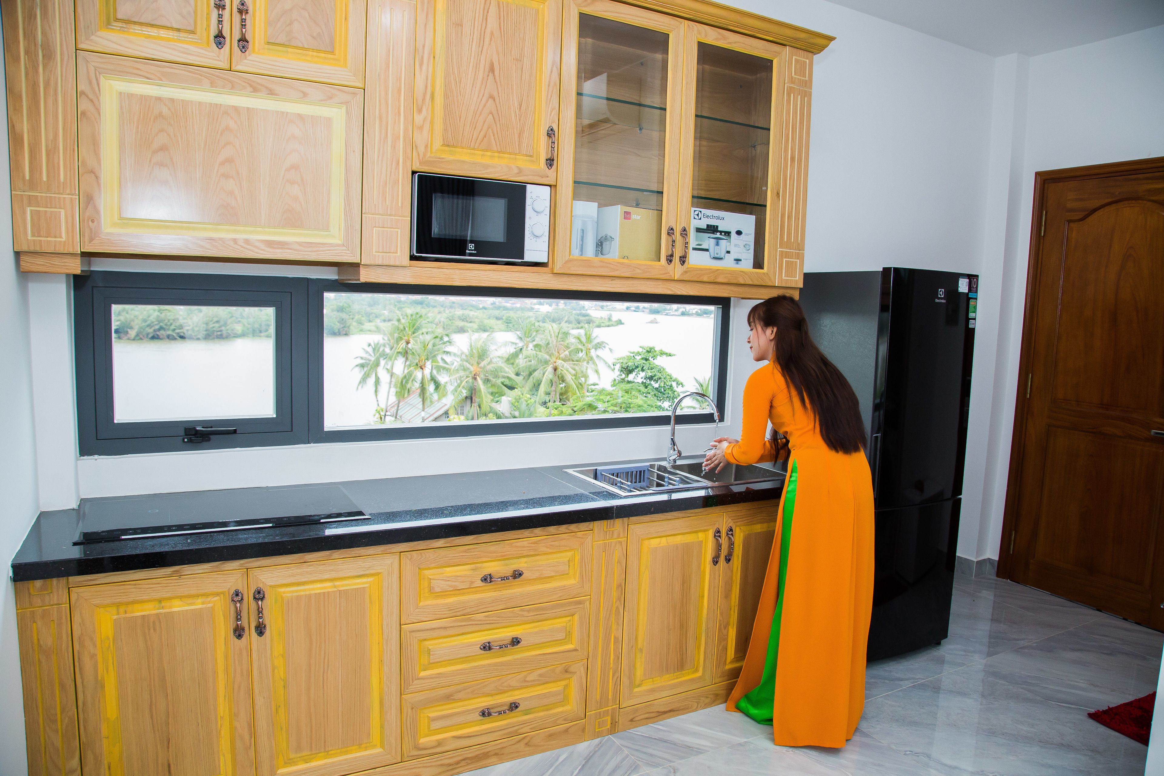 A kitchen with wooden cabinets, a black refrigerator, and a window with a view of greenery.