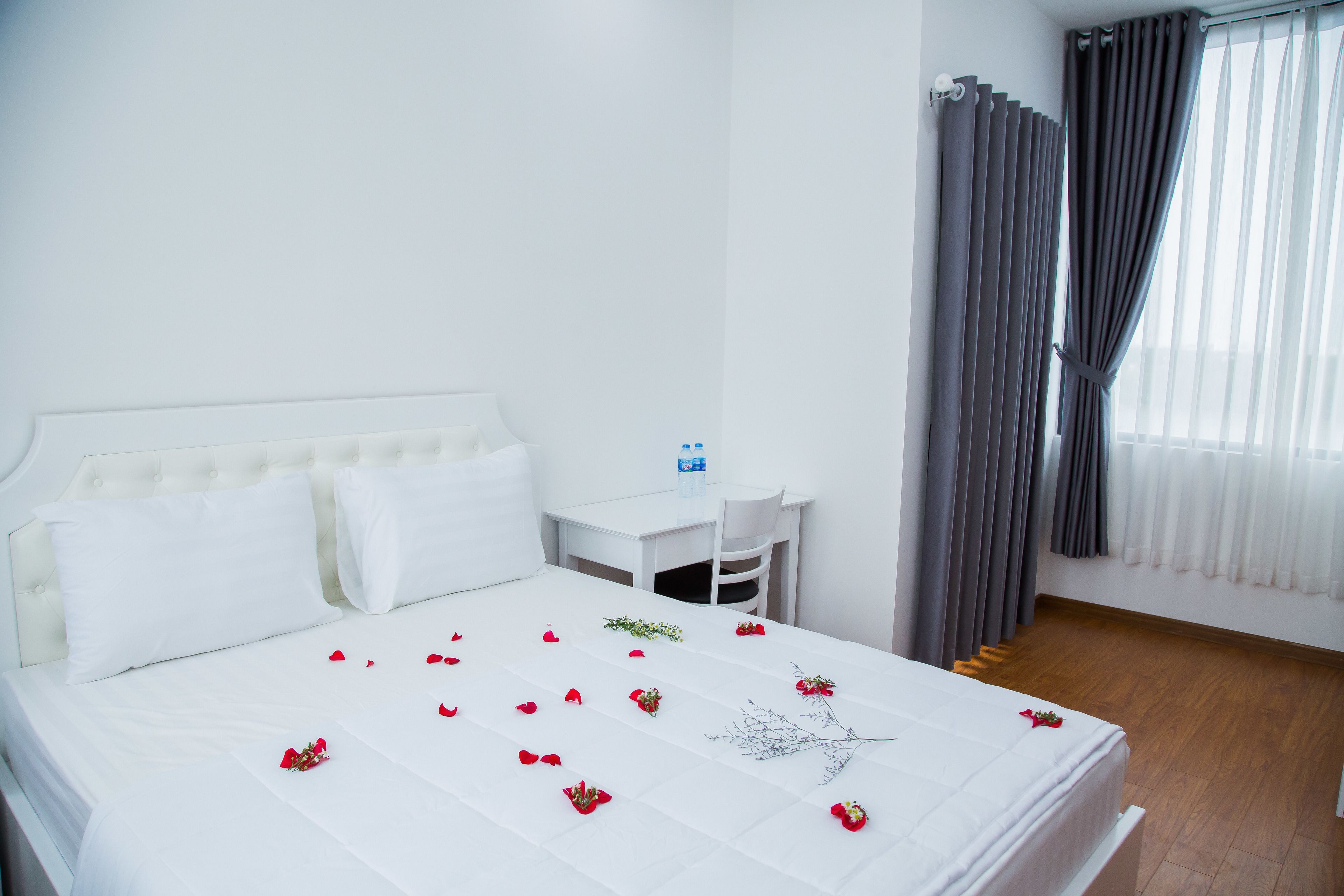 Une chambre d’hôtel avec un lit, une petite table et une chaise, une fenêtre avec des rideaux et un plancher en bois.