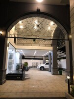 Una entrada con un arco de metal decorativo, una zona de estacionamiento techada y un automóvil blanco estacionado adentro.