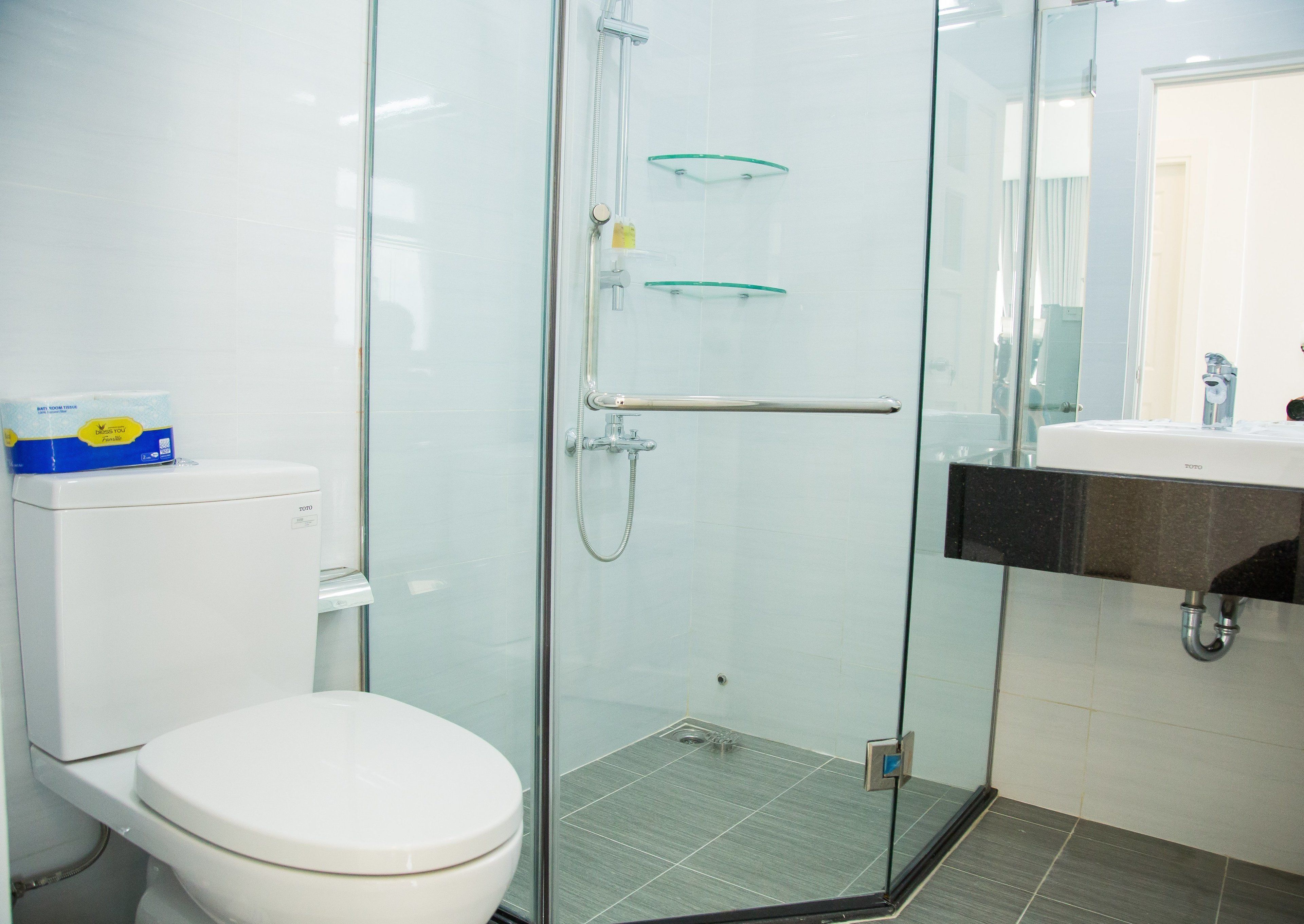 Un baño moderno con ducha envuelta en vidrio, inodoro blanco y lavamanos con encimera negra.