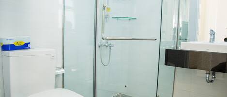 Un baño moderno con ducha envuelta en vidrio, inodoro blanco y lavamanos con encimera negra.
