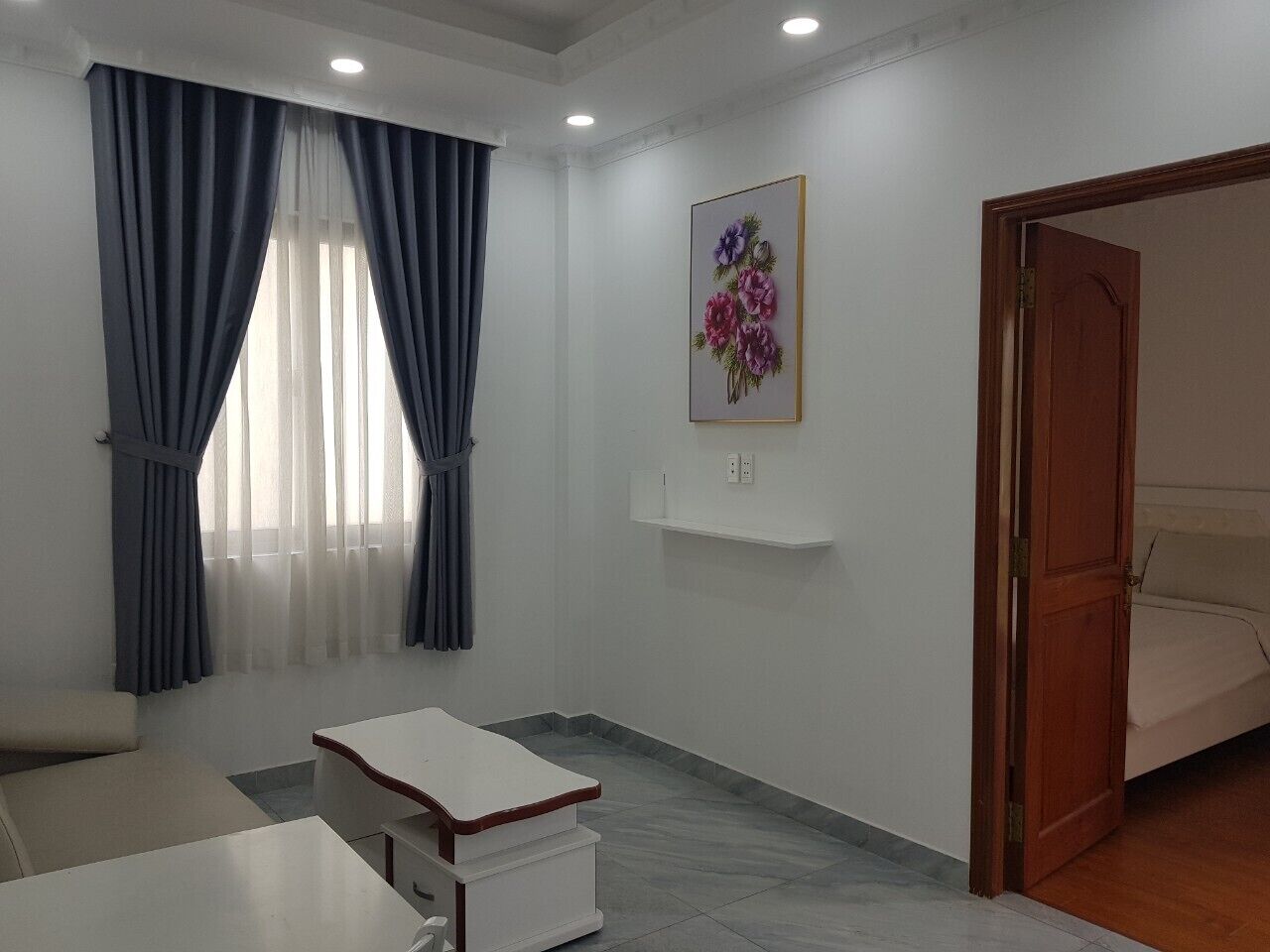A hotel room with a bed, a small table, a chair, a painting on the wall, and a door leading to another room.