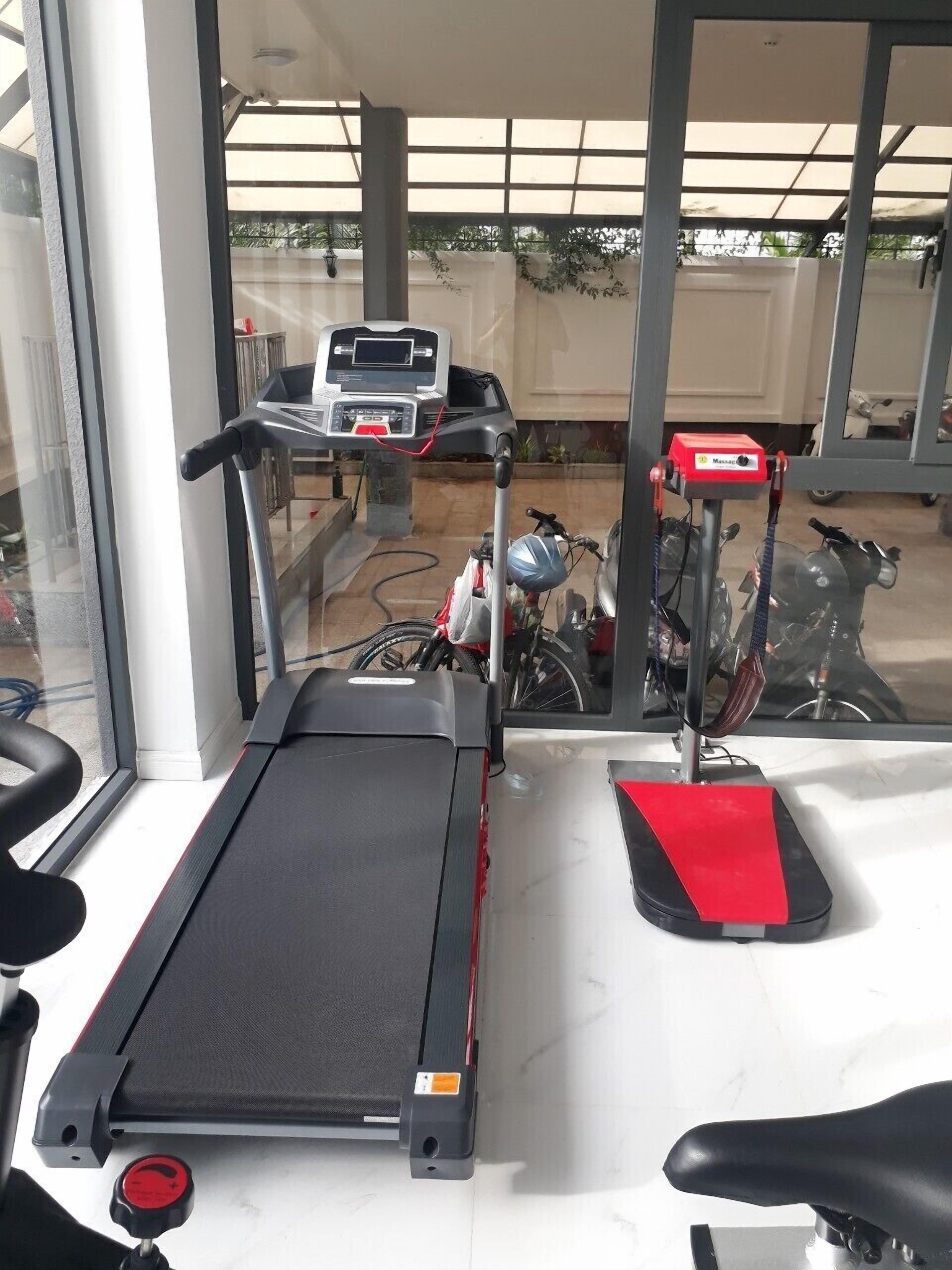 A treadmill in a room with large windows, a stationary bike, and a massage chair.