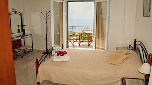 A bedroom with a bed, a dresser, a mirror, and an open balcony door leading to a terrace with a table and chairs. - Villa Fantasia (Kefalonia)