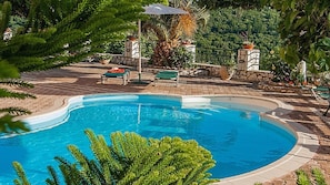 A swimming pool with a curved edge, surrounded by a stone deck and potted plants. - Villa Fantasia (Kefalonia)