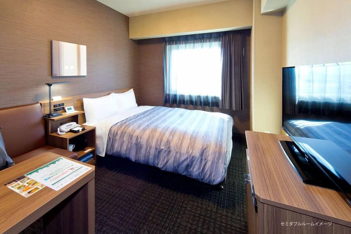 A hotel room with a bed, a desk, a TV, and a window with curtains.