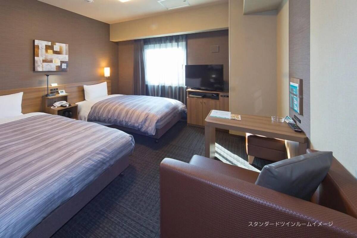 A hotel room with two beds, a desk, a chair, a TV, and a large mirror.