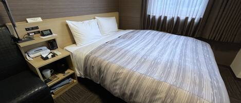 A hotel room with a large bed, a bedside table with a phone, a lamp, and a coffee maker.