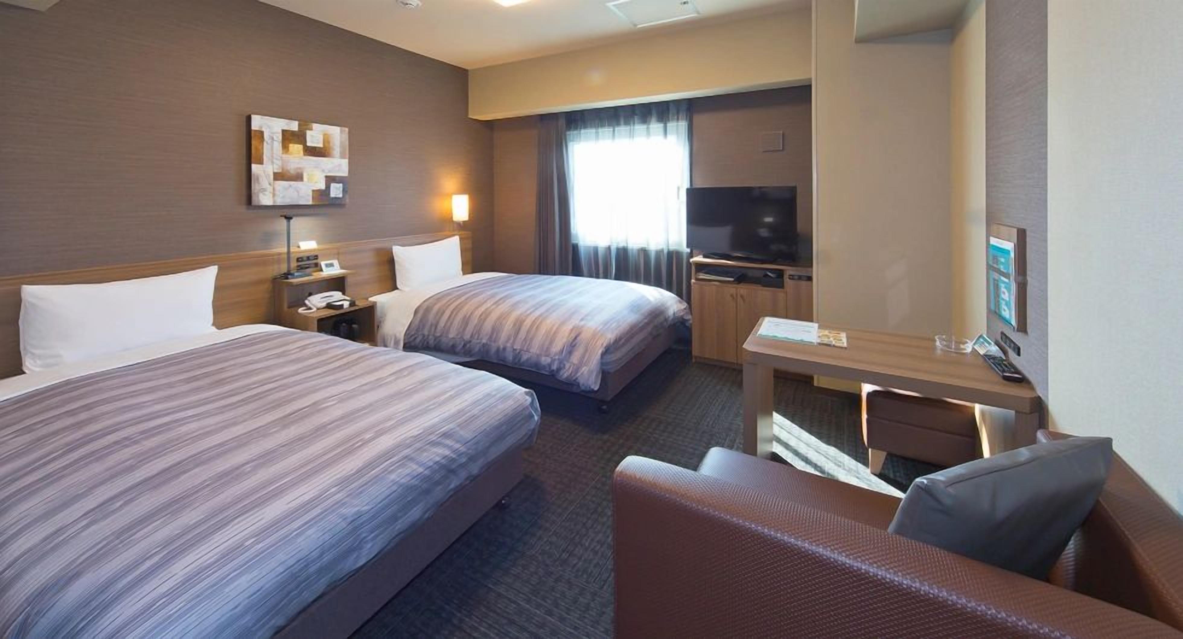 A hotel room with two beds, a desk, a chair, a TV, and a large mirror.