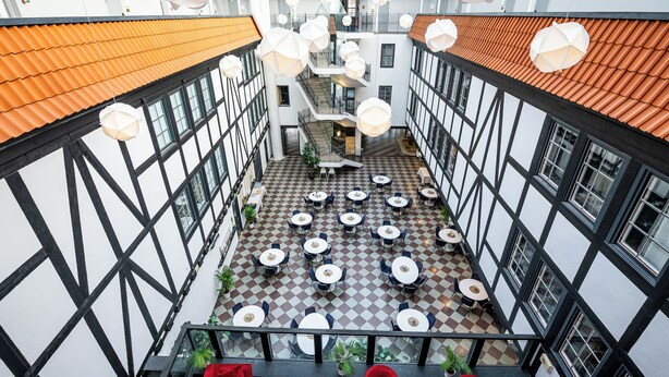 A multi-level atrium with a checkered floor, red seating, and multiple dining tables. - Hotel Stensson (Eslöv)