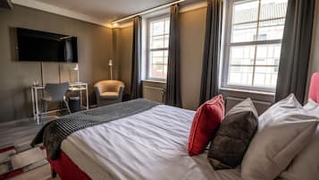 A hotel room with a bed, a desk, a chair, a TV, and large windows.