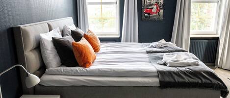 A modern bedroom with a large bed, a bedside table, and a window with curtains.