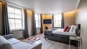 A modern hotel room with a large bed, a sofa, a TV mounted on the wall, and a window with curtains. - Hotel Stensson (Eslöv)