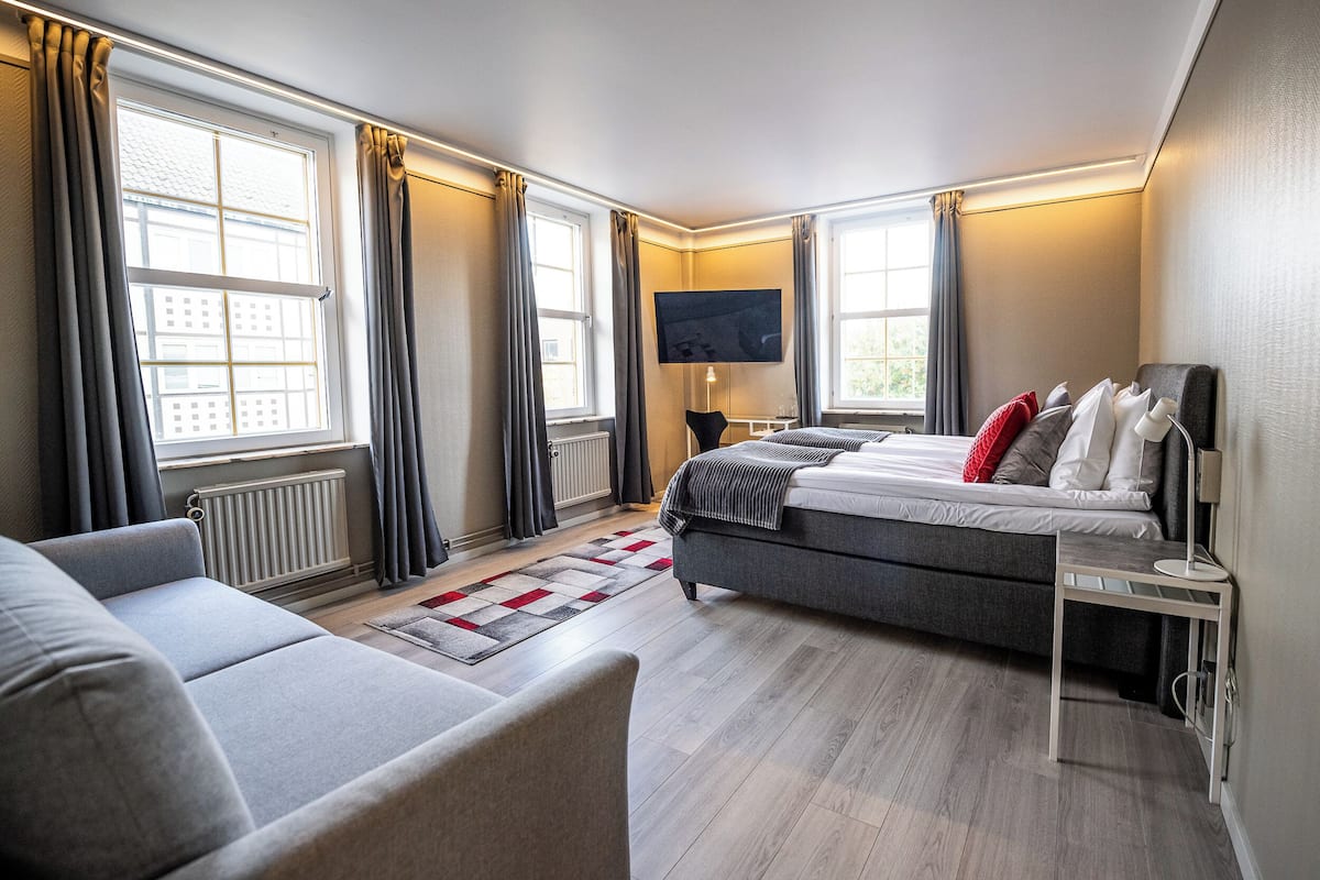 Une chambre d’hôtel moderne, dotée d’un grand lit, d’un canapé, d’un téléviseur fixé au mur et d’une fenêtre avec des rideaux.
