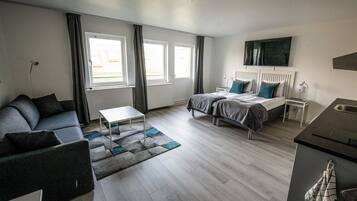 Een moderne hotelkamer met een bank, een bed met hoofdeinde, een kleine tafel en uitzicht op het exterieur door grote ramen.