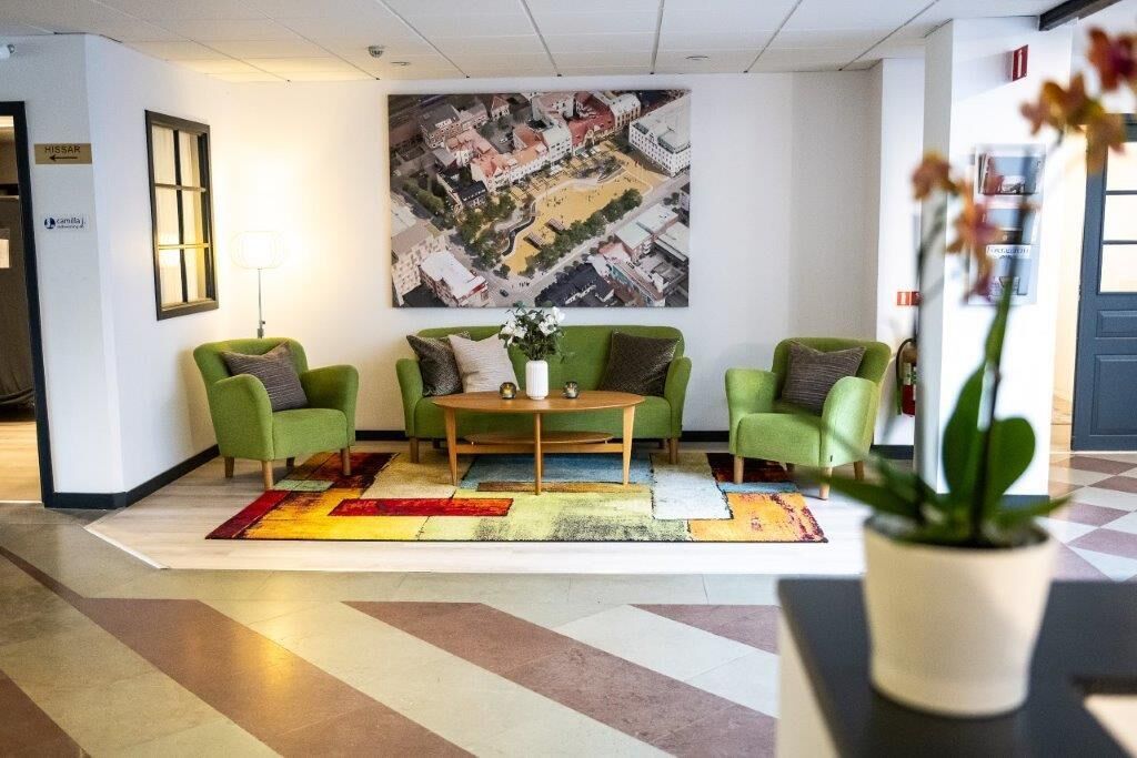 Un hall con sillones verdes, una mesa de centro y un cuadro grande con una vista panorámica de la ciudad.