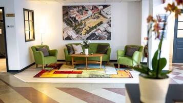 Un hall con sillones verdes, una mesa de centro y un cuadro grande con una vista panorámica de la ciudad.