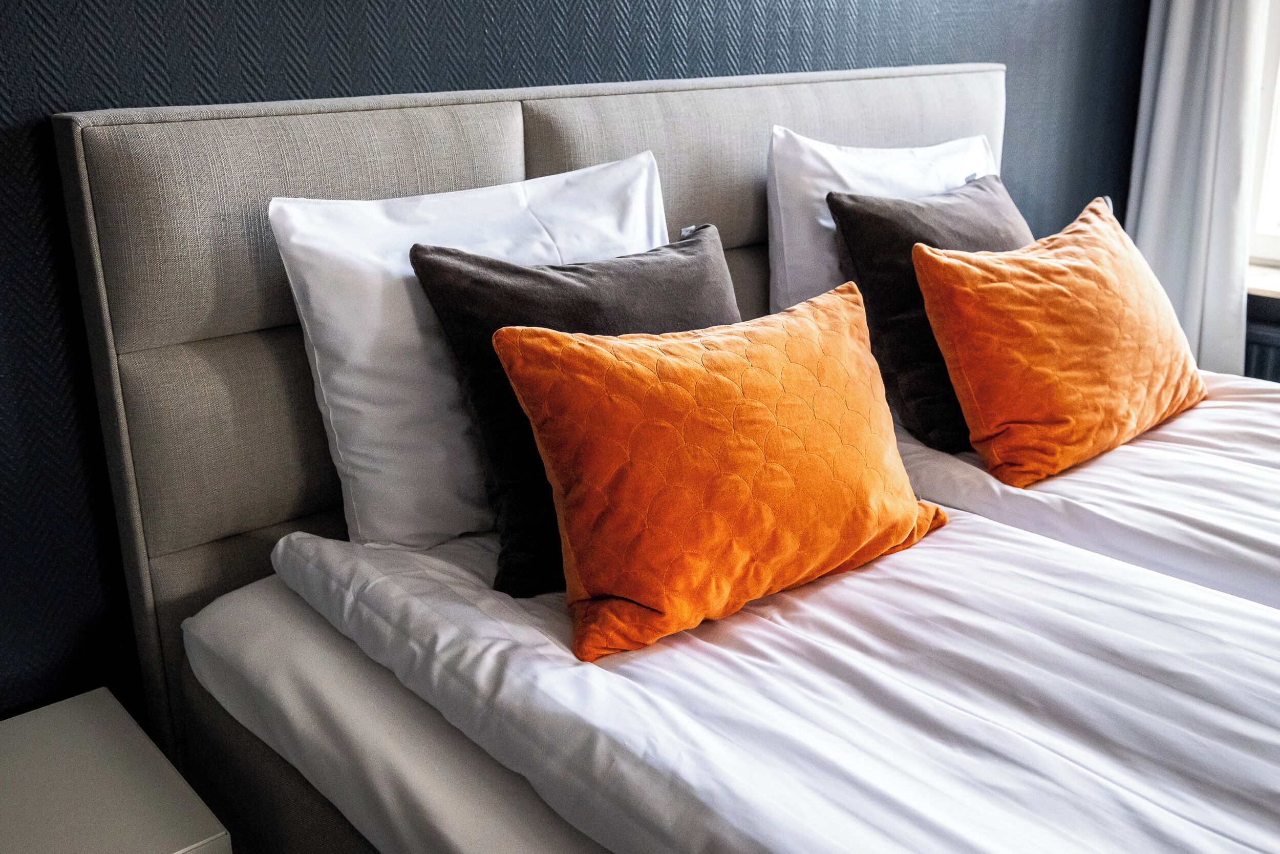 A neatly made bed with white linens and two orange pillows.