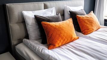 A neatly made bed with white linens and two orange pillows.