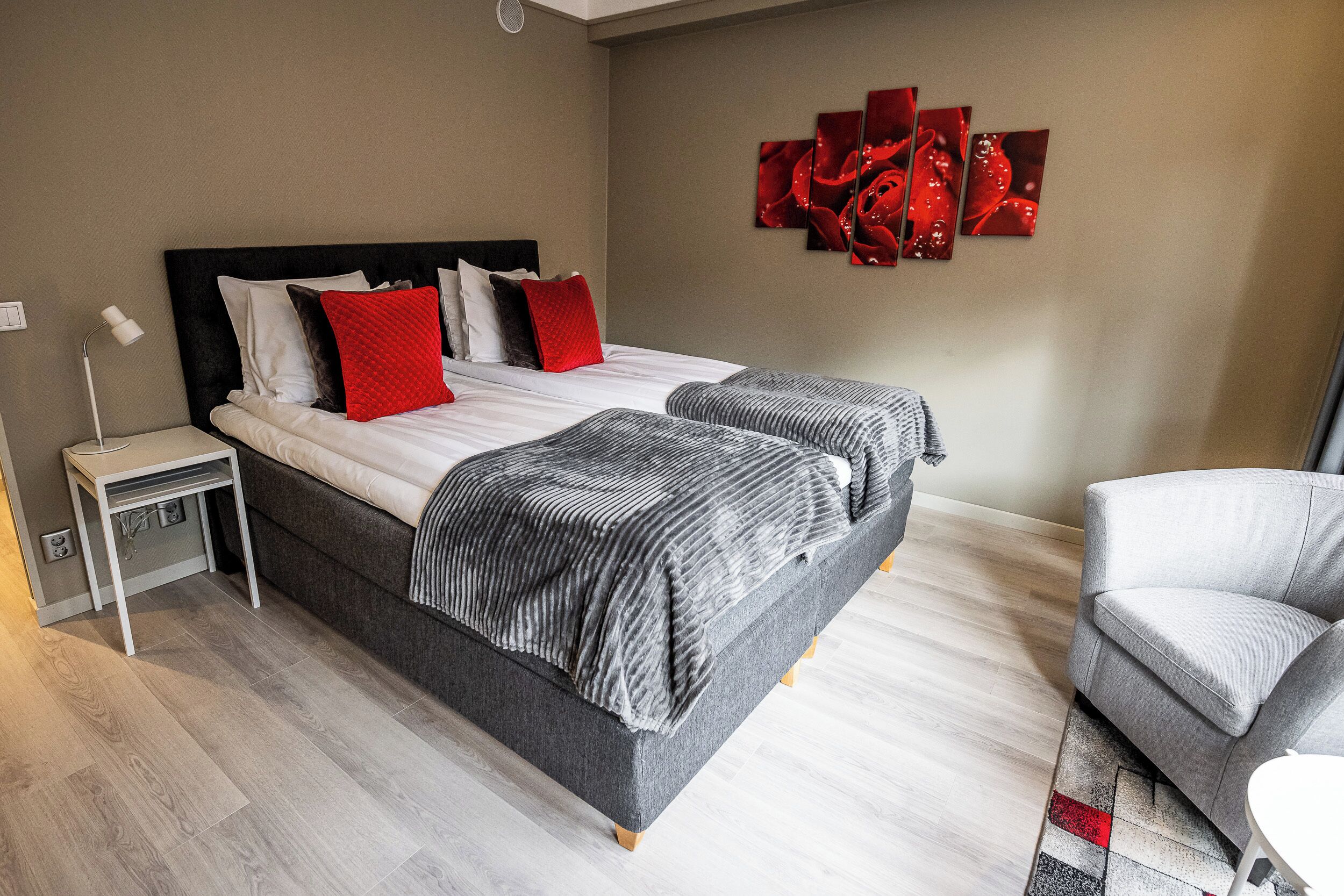 Un dormitorio moderno con una cama doble, dos mesitas de noche, un sillón gris y una obra de arte abstracto roja en la pared.