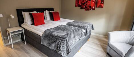 Un dormitorio moderno con una cama doble, dos mesitas de noche, un sillón gris y una obra de arte abstracto roja en la pared.