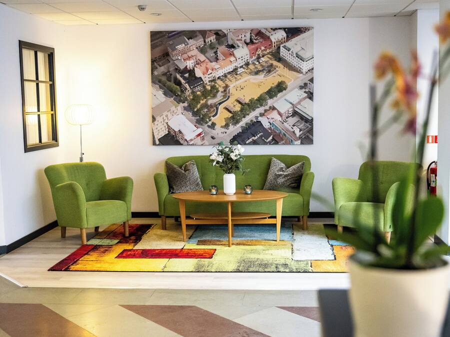 Un hall con un sofá verde, una mesa de centro, una alfombra colorida y un cuadro grande de un paisaje urbano en la pared.