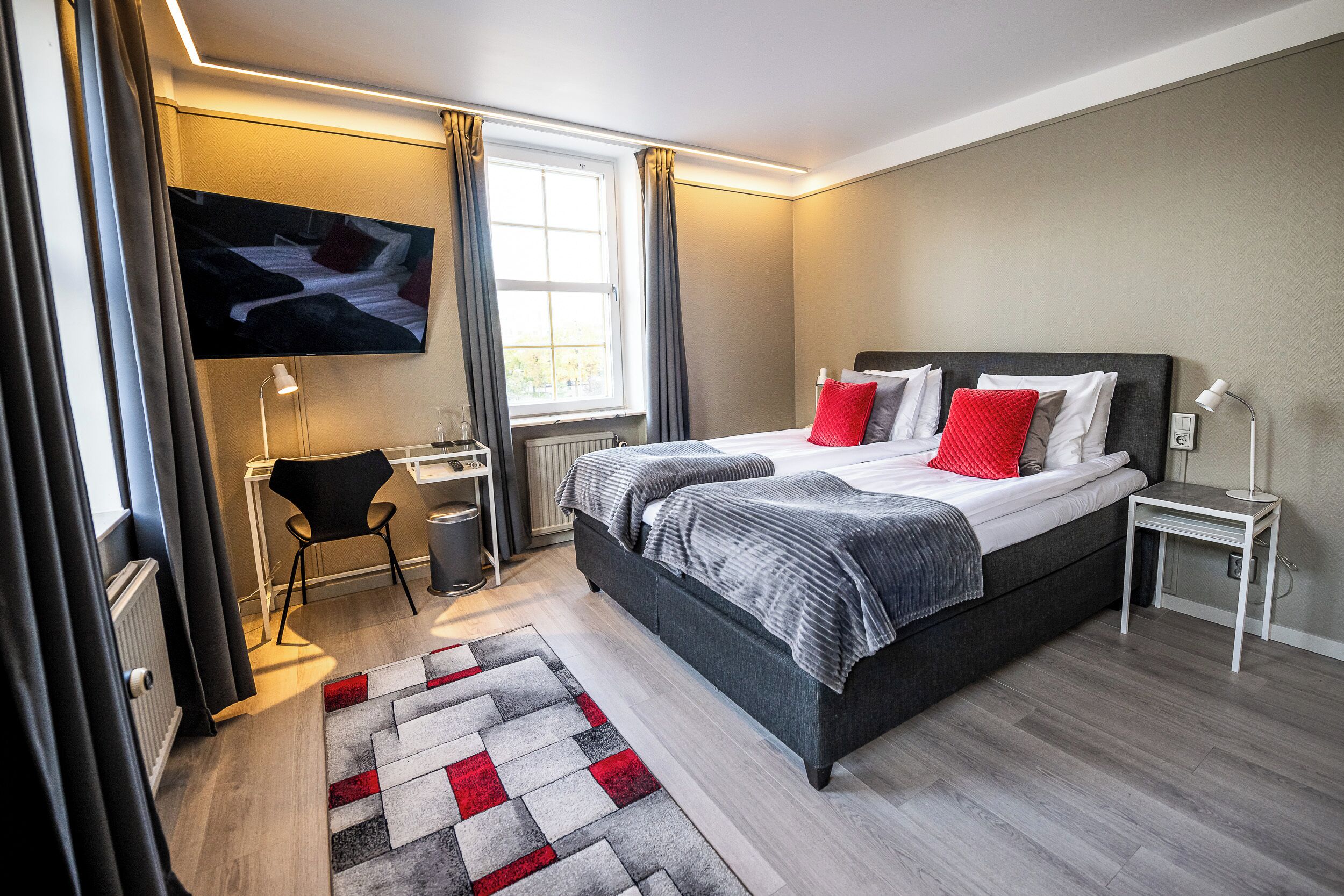 Une chambre d’hôtel moderne avec un grand lit, un bureau et un téléviseur fixé au mur.
