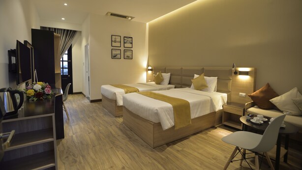 A hotel room with two beds, a desk, a chair, and a small table with cups and a teapot. - 7s Hotel An Phú Central (Ho Chi Minh City)