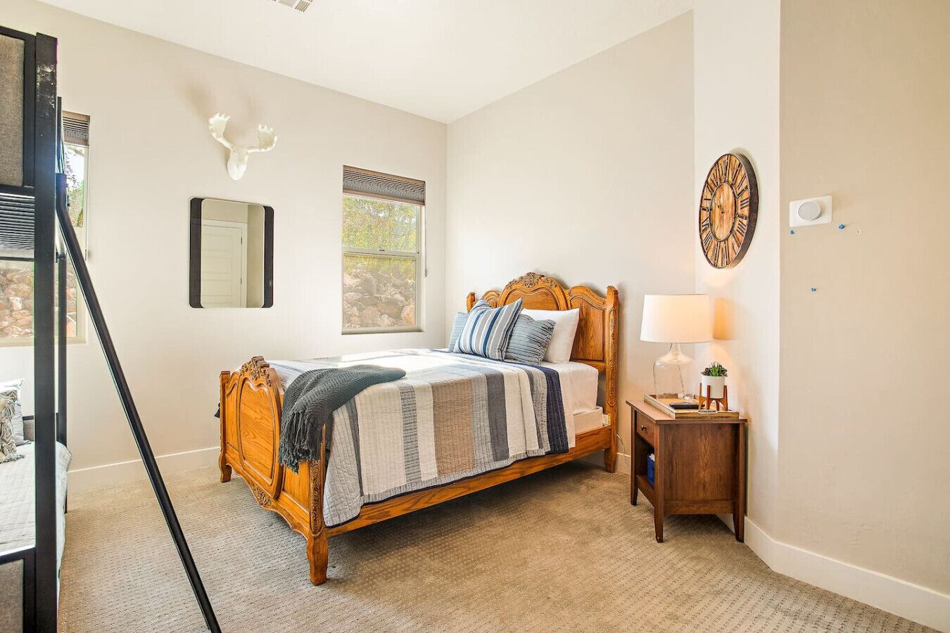 Een slaapkamer met een houten bed, een nachtkastje met een lamp, een wandklok en een raam met jaloezieën.