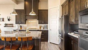 A kitchen with dark wood cabinets, a stainless steel refrigerator, a double oven, and a marble island with bar stools.