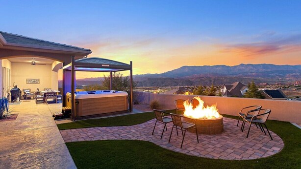 A patio with a hot tub, fire pit, and outdoor seating area with a view of mountains.
