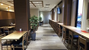 A restaurant with long wooden tables and chairs, potted plants, and a TV mounted on the wall.