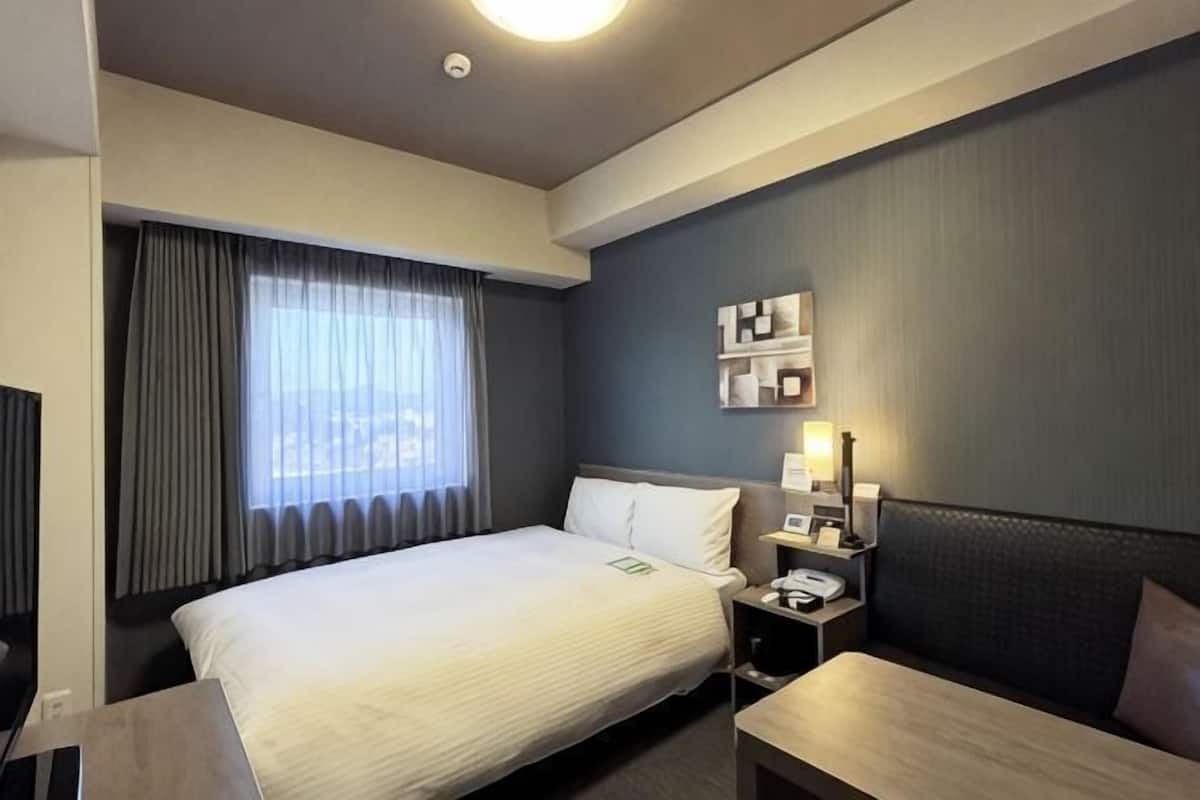 Ein Hotelzimmer mit Bett, Nachttisch, Lampe und einer kleinen Sitzecke.