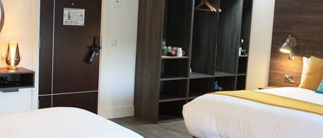 A hotel room with two beds, a wardrobe, a desk, and a bedside lamp.