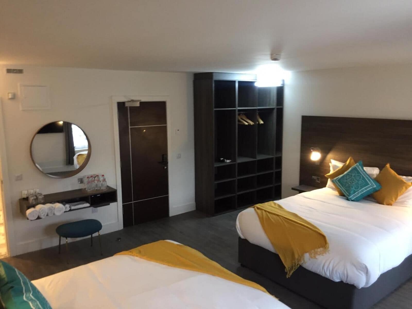 Hotellihuoneessa on suuri sänky, pienempi sänky, vaatekaappi, peili ja hylly, jossa on hygieniatuotteita.