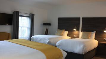 A hotel room with two beds, a TV, a lamp, and a window with curtains.