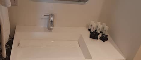 A bathroom with a white sink, a mirror, and a shelf with towels and toiletries.