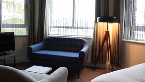 A hotel room with a blue sofa, a bedside table with a lamp, and a TV. - Base Accommodation Dingle (Dingle)