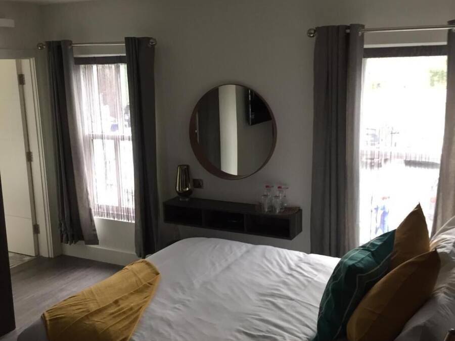 A hotel room with a large bed, a round mirror, a small shelf with toiletries, and a view through the window.