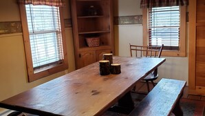 A dining area with a wooden table, benches, and chairs. There is a wooden bookshelf with a basket and a decorative item on the lower shelf. - RIVERVIEW ADIRONDACK RUSTIC APARTMENT (Warrensburg)